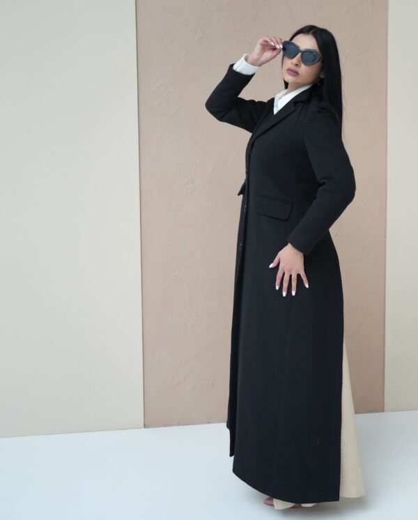 midnight-black-mantle-side-view – Woman modeling a sleek black mantle coat with sharp tailoring.